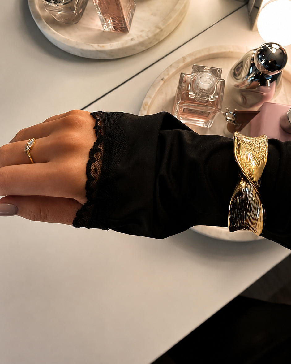 Bredt guldfarvet armbånd på et håndled med sort bluse