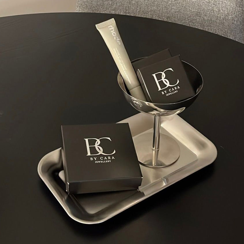 By Cara Jewellery smykkeæsker og læbeprodukt præsenteret på sort bord i elegant gaveopsætning