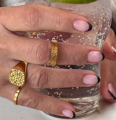 Hånd med guldbelagte ringe med struktureret overflade, holdt om glas med is og bobler